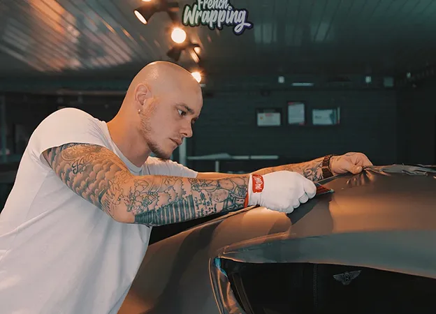 Homme chauve et tatoué enveloppant une voiture en noir mat à Maisons-Laffitte dans les Yvelines 78