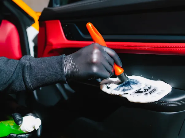 Main gantée nettoyant la garniture de portière de voiture noire avec brosse et mousse à Maisons-Laffitte dans les Yvelines 78