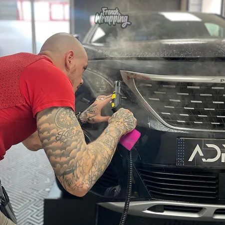 Homme tatoué appliquant un film protecteur sur le pare-chocs d'une voiture noire à Maisons-Laffitte dans les Yvelines 78