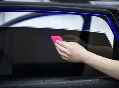 Main qui applique un film teinté sur une vitre de voiture avec une raclette à Maisons-Laffitte dans les Yvelines 78