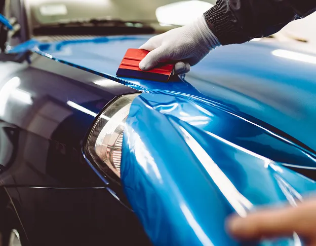 Une main gantée applique une pellicule bleue brillante sur le capot d'une voiture à Maisons-Laffite dans les Yvelines 78