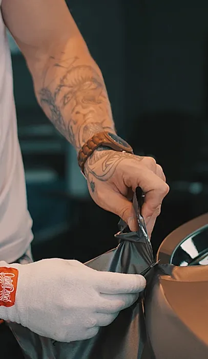 Mains gantées appliquant un film vinyle foncé sur une voiture bronze à Maisons-Laffite dans les Yvelines 78