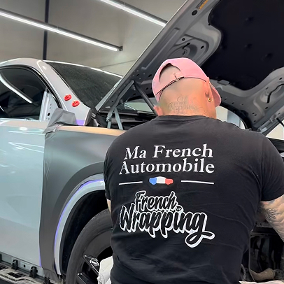 Homme en casquette rose et t-shirt noir travaillant sur une voiture.
