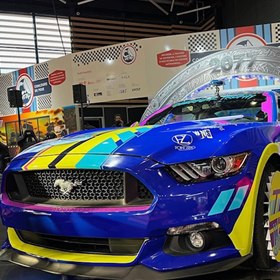 Ford Mustang bleue vivement colorée avec des bandes jaunes et roses, présentée à un événement.