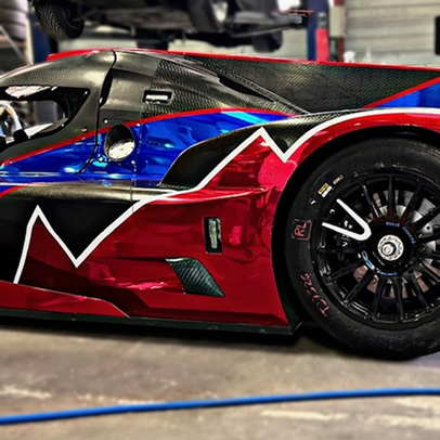 Voiture de course rouge, bleue et noire en fibre de carbone dans un garage.