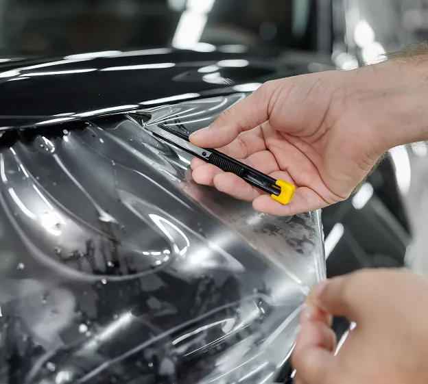 Main tenant un cutter, coupant un film protecteur transparent sur une voiture noire à Maisons-Laffitte dans les Yvelines 78