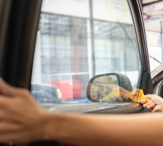 Application de film teinté sur une vitre de voiture avec une raclette jaune à Maisons-Laffitte dans les Yvelines 78