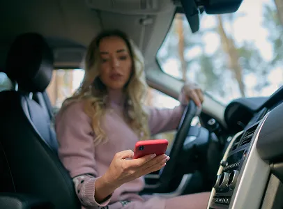 Femme blonde dans une voiture, conduisant et regardant son téléphone rouge à Maisons-Laffitte dans les Yvelines 78